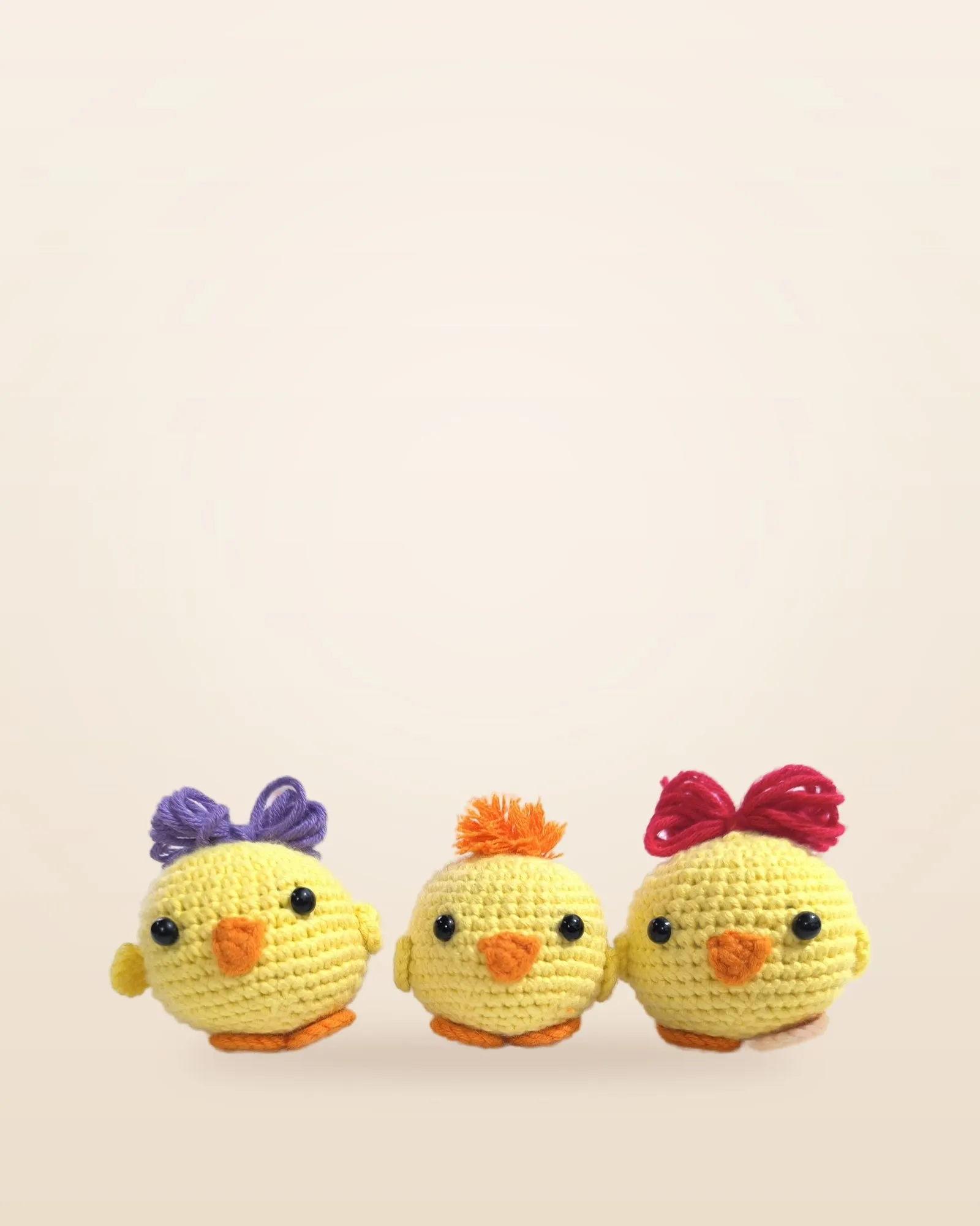 Tres pollitos amarillos de crochet con moños lila, naranja y rojo